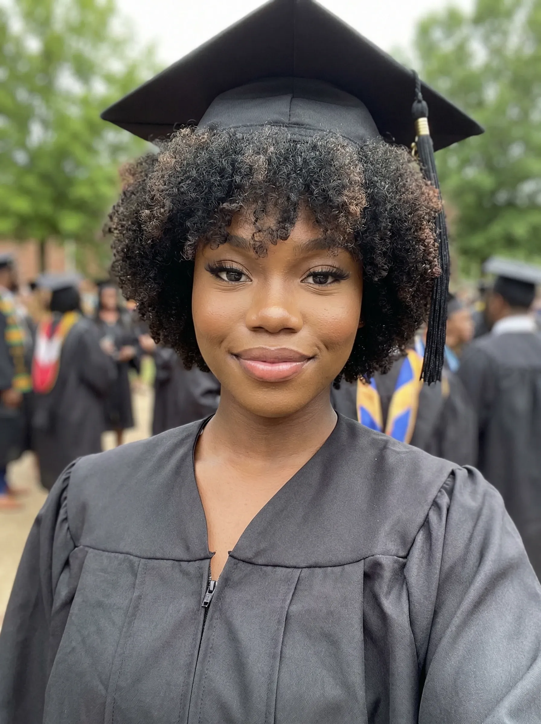 AI graduation headshot — woman in cap and gown at an outdoor commencement ceremony